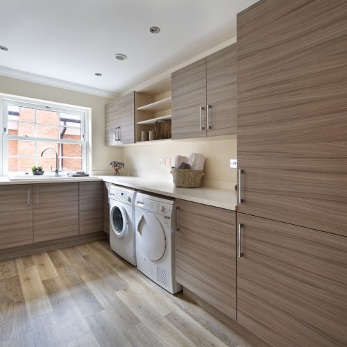 a lovely utility room in a large modern new home with ample cupboard space, work-top space and separate washing machine and dryer. The flooring is a high quality porcelain oak-wood effect tile which looks completely natural. The room has been lightly dressed for this image.