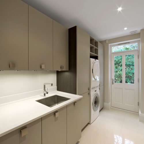 "a utility room in an expenbsive new home with stacked washer and drier, loads of cupboards, a worktop with sink and hot / cold water. The cupboard doors are caramel coloured and the floor lined with marble tiles.Looking for a Kitchen, Dining Room or dining related image Then please see my other images by clicking on the Lightbox link below..."